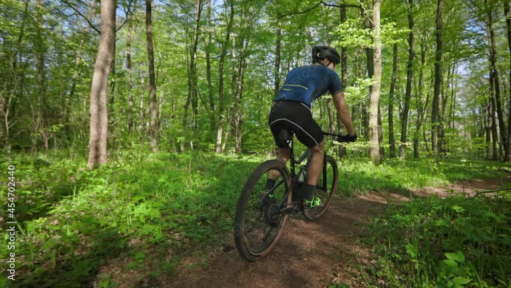 A cyclist is riding along a forest path. He is making turns. The camera is moving around him. The sun is shining through the trees. 4K A cyclist is riding along a forest path. He is making turns. The camera is moving around him. The sun is shining through the trees. 4K