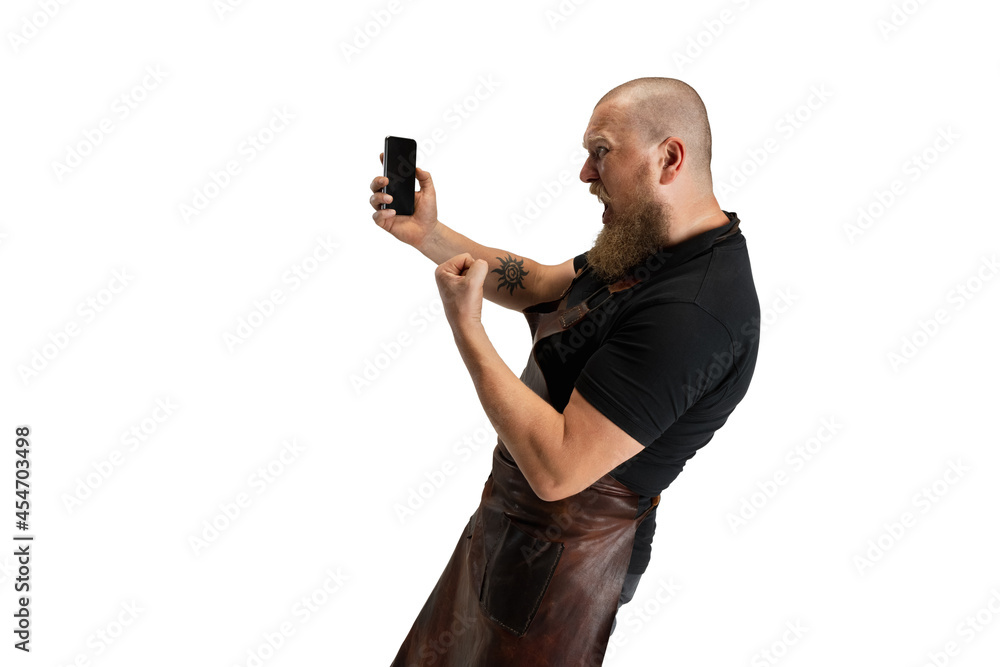 Comic portrait of muscular bearded bald man, blacksmith in leather apron or uniform isolated on white studio background. Concept of labor, retro professions, power, beauty, humor Comic portrait of muscular bearded bald man, blacksmith in leather apron or uniform isolated on white studio background. Concept of labor, retro professions, power, beauty, humor