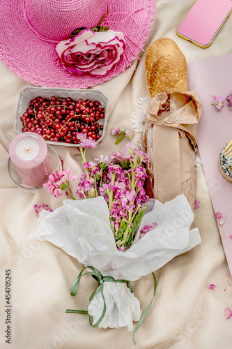 Pink hat with baguette , bunch of flowers and fruits on picnic blanket. Top view. Outdoor.