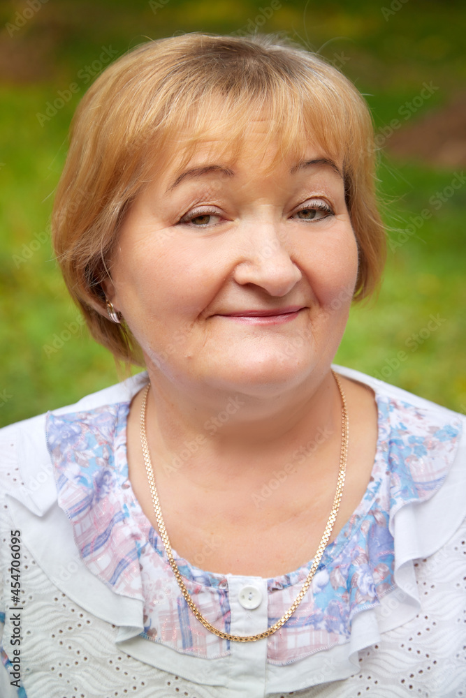 Portrait of an elderly or middle-aged woman with a green background in a park or forest in nature Portrait of an elderly or middle-aged woman with a green background in a park or forest in nature