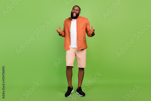 Full body photo of optimistic millennial brunet guy sing wear shirt shorts shoes isolated on green background