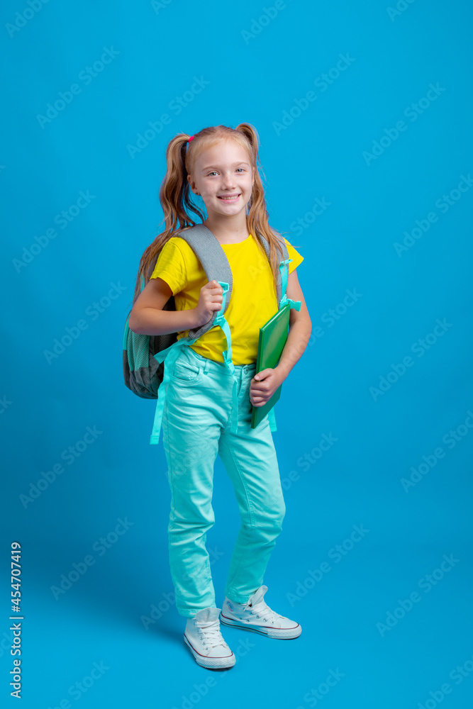 a little girl with a backpack holds a book on a blue background a little girl with a backpack holds a book on a blue background
