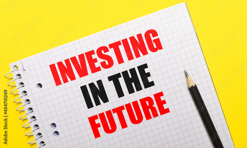 White notebook with inscription INVESTING IN THE FUTURE written in black pencil on a bright yellow background. White notebook with inscription INVESTING IN THE FUTURE written in black pencil on a bright yellow background.