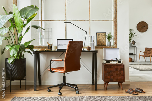 Creative composition of modern masculine home office workspace interior with black industrial desk, brown leather armchair, laptop, vintage record player and stylish personal accessories. Template.