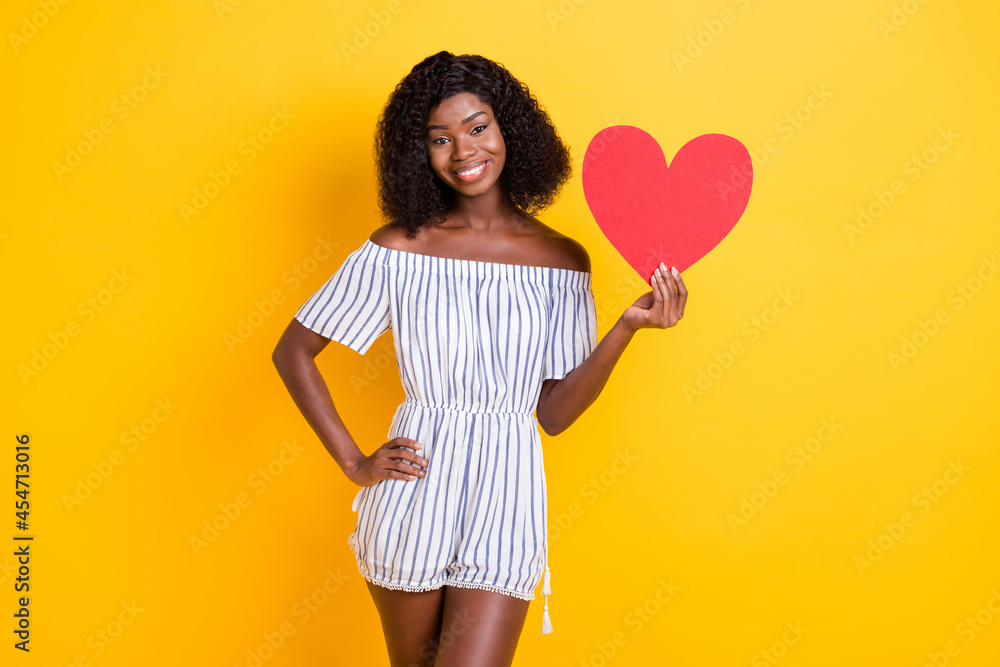 Portrait of attractive cheerful girl holding in hand heart card congrats isolated over bright yellow color background Portrait of attractive cheerful girl holding in hand heart card congrats isolated over bright yellow color background