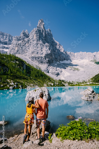 Morning with clear sky on Lago di Sorapis in the Italian Dolomites, milky blue lake Lago di Sorapis, Lake Sorapis, Dolomites, Italy. Couple man and woman mid age walking by the lake in the mountains  photo