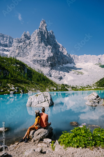 Morning with clear sky on Lago di Sorapis in the Italian Dolomites, milky blue lake Lago di Sorapis, Lake Sorapis, Dolomites, Italy. Couple man and woman mid age walking by the lake in the mountains  photo