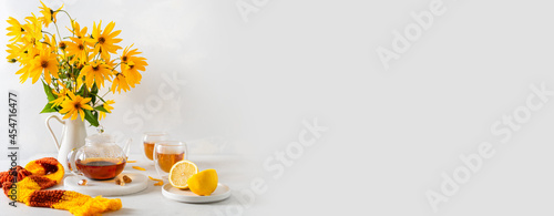Cozy autumn banner. Hot teapot, two cups of tea, yellow flowers bouquet, lemon and knitted scarf on white background side view. Autumn, fall, tea party concept. Restaurant Web line, sale. Copy space © Dina Photo Stories