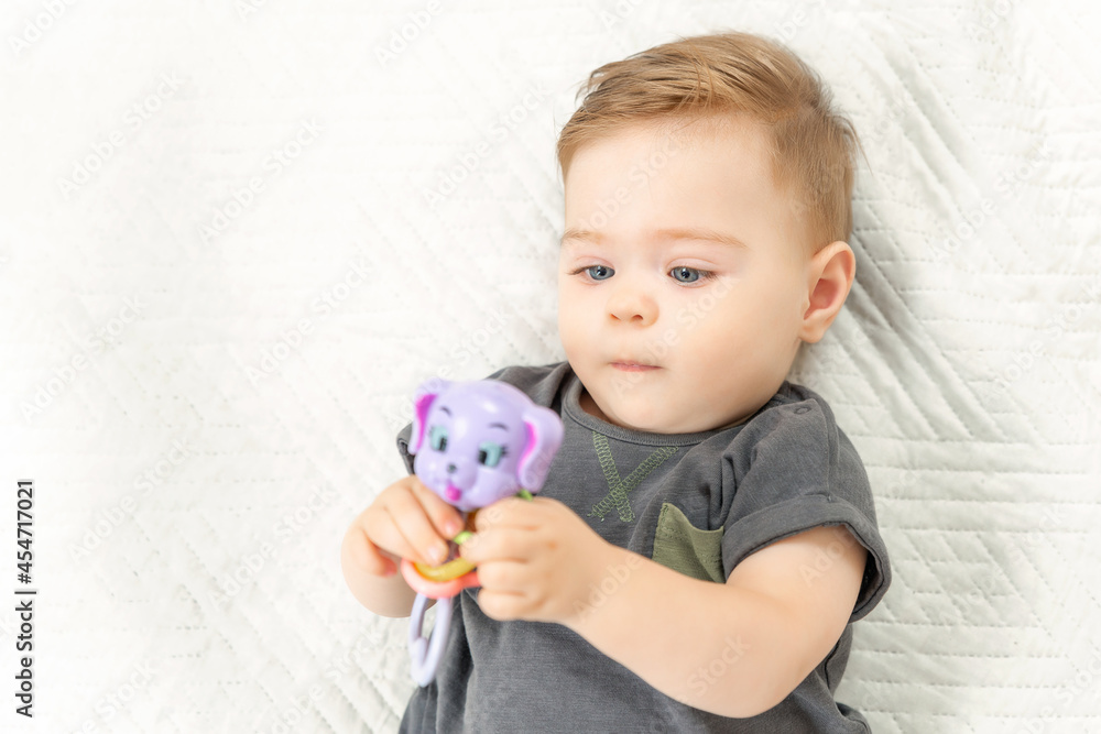 Curious little baby child with rattle toy lying on bed in a sunny bedroom. Curious little baby child with rattle toy lying on bed in a sunny bedroom.