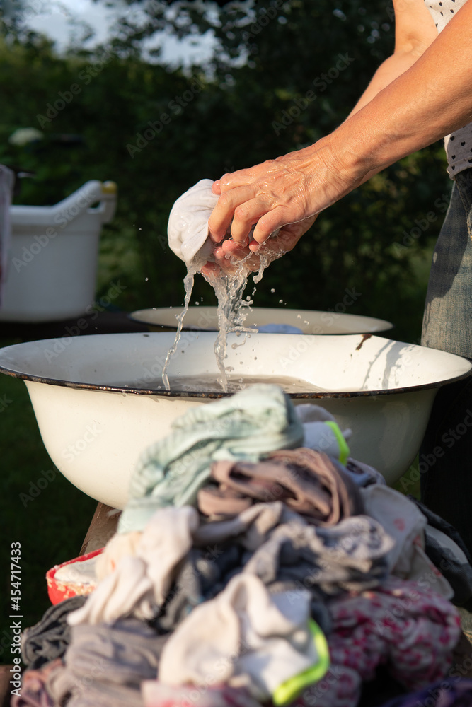 Woman washes clothes with her hands in old basin with a soap outdoors