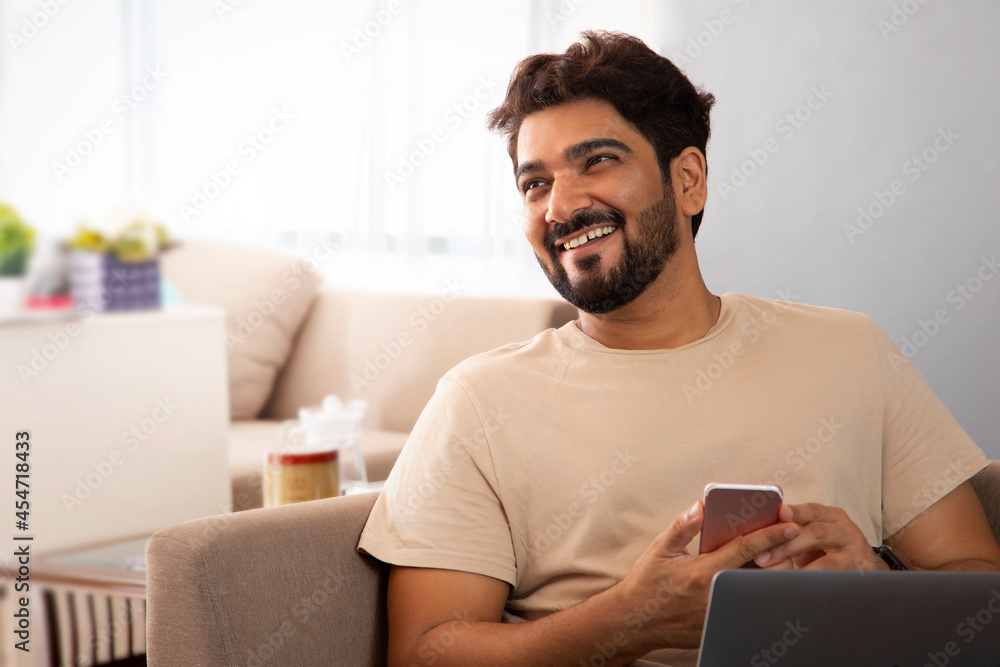 A man sitting with laptop holding his mobile looking sideways. A man sitting with laptop holding his mobile looking sideways.