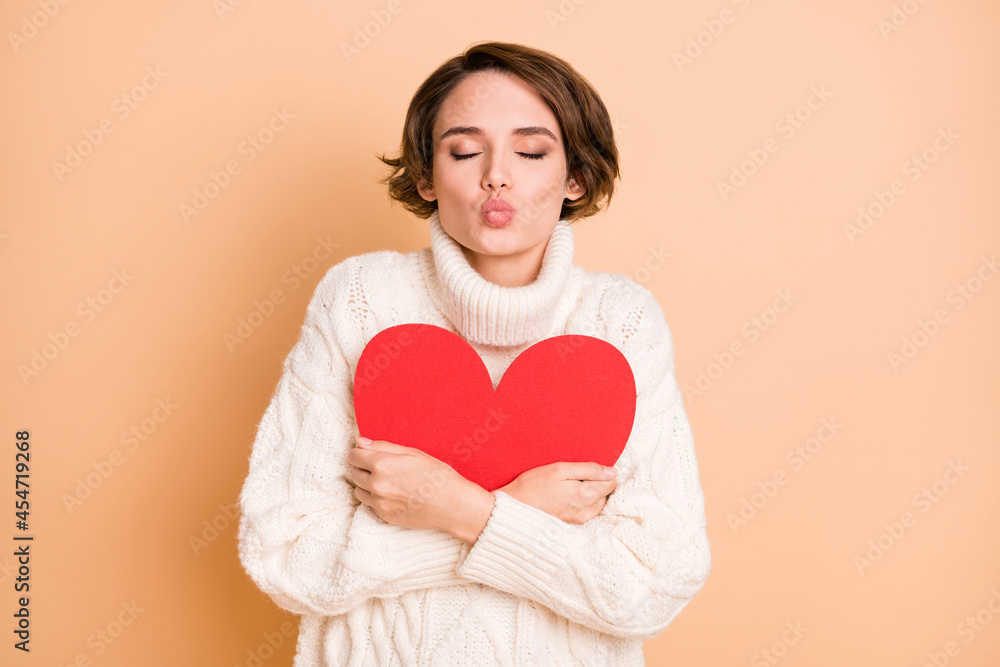 Photo of lovely charming young woman hug red paper heart send air kiss isolated on beige color background Photo of lovely charming young woman hug red paper heart send air kiss isolated on beige color background