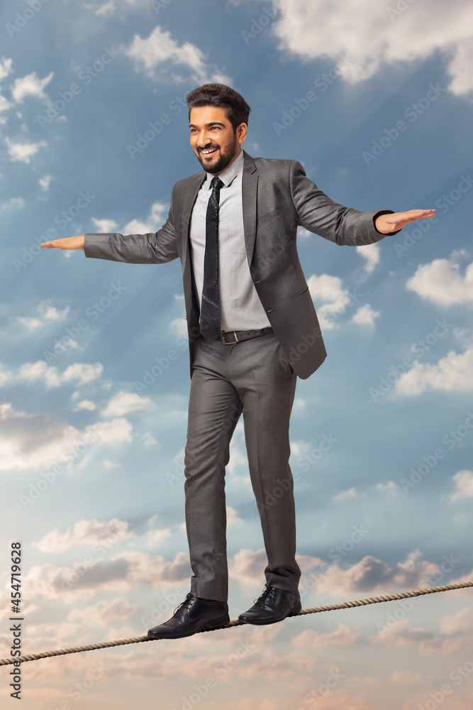  A man in formal business suit walking with hands stretched on a rope.