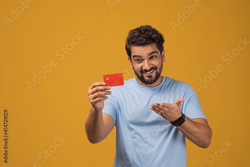 Portrait of a man showing  the credit card in his hand against plain background. © IndiaPix