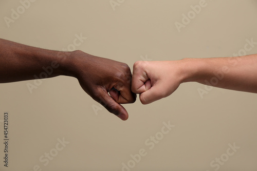 Men making fist bump on beige background, closeup photo