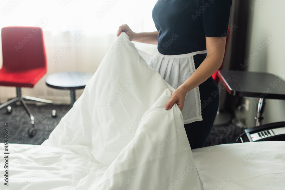 cropped view of young chambermaid in uniform changing bedding in hotel room cropped view of young chambermaid in uniform changing bedding in hotel room