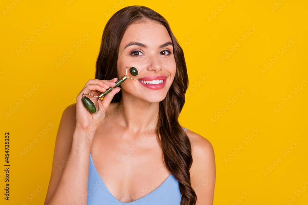 Photo of young attractive woman happy positive smile use roller massager skincare isolated over yellow color background Photo of young attractive woman happy positive smile use roller massager skincare isolated over yellow color background