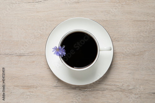 Cup of delicious chicory drink and flowers on light wooden table, top view
