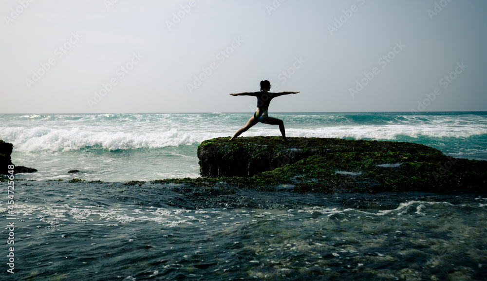 Woman practice yoga at seaside cliff edge facing the coming strong sea waves