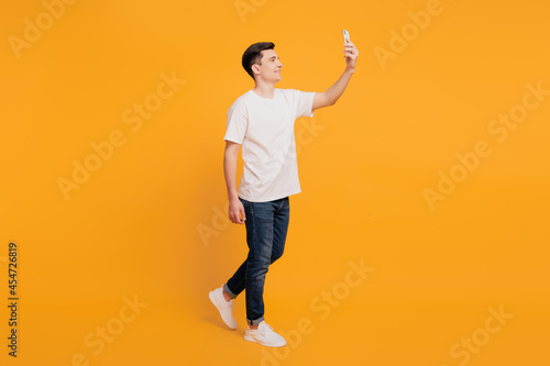 Portrait of positive handsome guy take selfie hold phone walk on yellow background