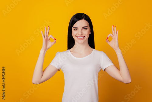 Photo of attractive cheerful young girl showing okay sign advert solution isolated over bright yellow color background