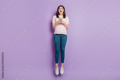 Fototapeta Naklejka Na Ścianę i Meble -  Portrait of funky carefree energetic lady hold cellphone jump have fun on violet background