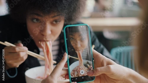 beautiful african american woman eating spaghetti at restaurant with friend using smartphone taking photo having fun sharing weekend together on social media 4k