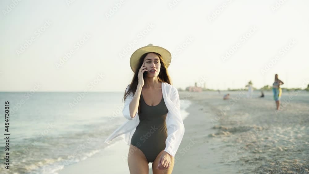 Caucasian lady on vacation walks along the sandy beach, holds a phone in her hands and makes a call. Caucasian lady on vacation walks along the sandy beach, holds a phone in her hands and makes a call.