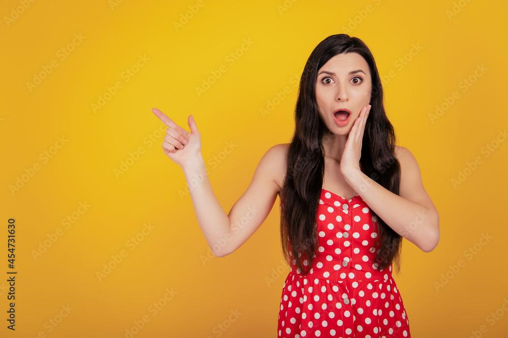 Portrait of crazy woman finger show up empty space open mouth palm cheek wear dotted red dress on yellow background Portrait of crazy woman finger show up empty space open mouth palm cheek wear dotted red dress on yellow background