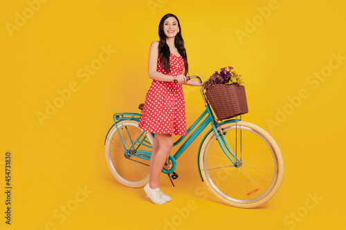 Portrait of cheerful lady ride bike look camera posing wear dotted red dress on yellow background © Tetiana