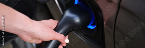 Woman hand refueling car with electricity using cable closeup