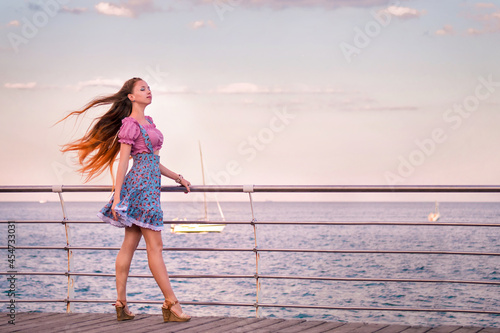 Beautiful red-haired girl with long hair fluttering in the wind, walk by the sea, relax