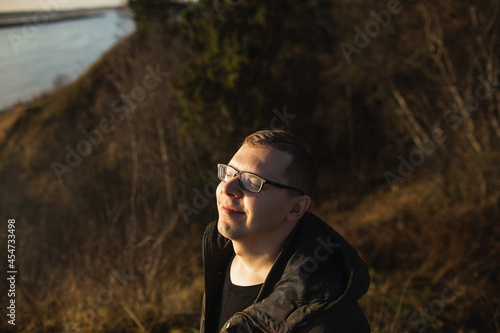 A young man in glasses enjoys the beautiful autumn nature on a sunny autumn day in the forest