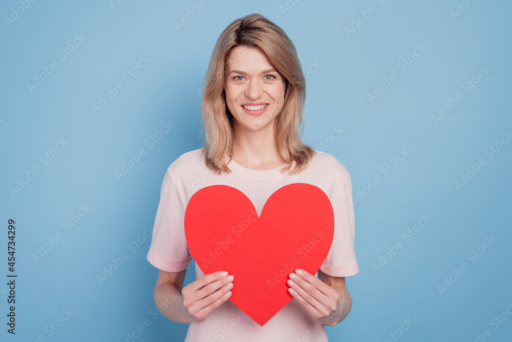 Portrait of pretty lovely sweet girl hands hold red paper heart figure card on blue background Portrait of pretty lovely sweet girl hands hold red paper heart figure card on blue background