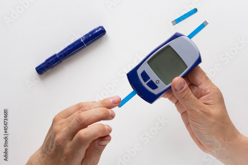 Top view of woman hand holding glucose meter with test strip in it and putting drop of blood on test strip photo