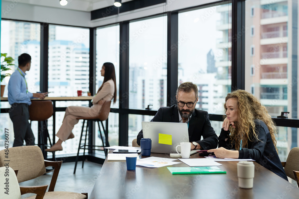 Businessman and businesswoman working laptop computer and tablet in the office with city blur background Businessman and businesswoman working laptop computer and tablet in the office with city blur background