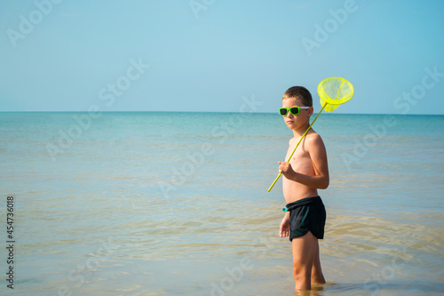 boy in sunglasses stands in the sea with a butterfly net.