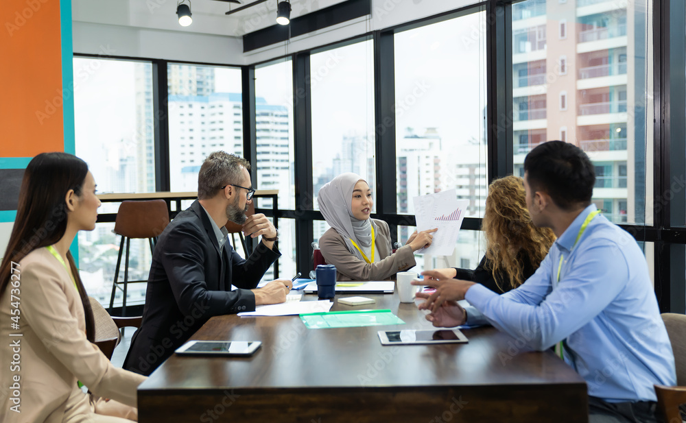 Asian Muslim business woman in hijab headscarf sitting on wheelchair presenting of her work to corporate colleagues in meeting in the modern office. diverse corporate colleagues and multicultural Asian Muslim business woman in hijab headscarf sitting on wheelchair presenting of her work to corporate colleagues in meeting in the modern office. diverse corporate colleagues and multicultural