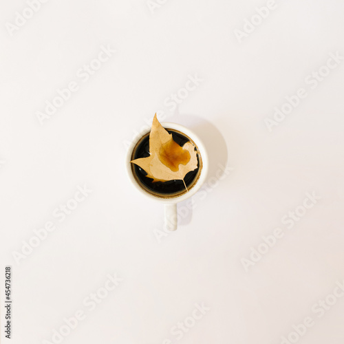 cup of coffee with yellow gold autumn leaf in the middle.white background nature minimal art concept photo