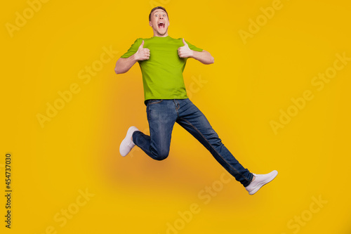 Full length photo of nice attractive cheerful optimistic guy show thum-up like cool jump up isolated over yellow background