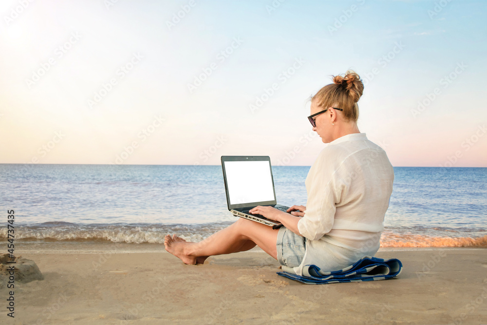 young woman freelancer works at the seaside. woman with laptop computer on the beach.