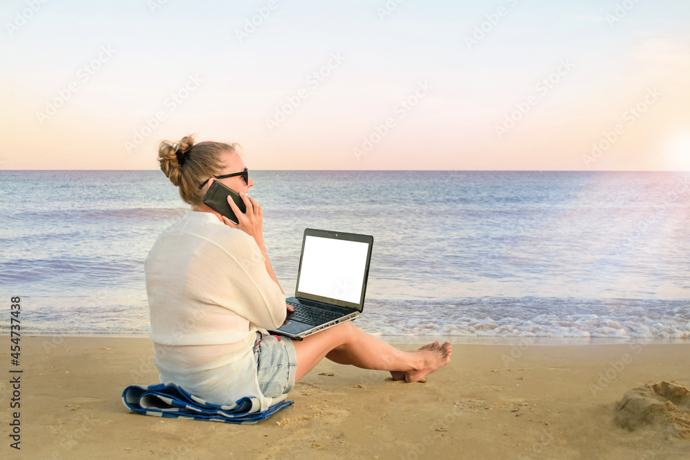 young woman freelancer works at the seaside. woman talking on a mobile phone, with a laptop computer in her hands, on the beach.