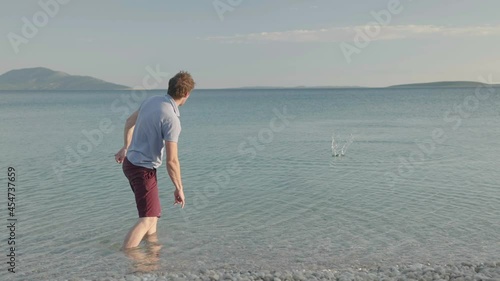 Slow motion - Young adult caucasian man skipping stone on water photo