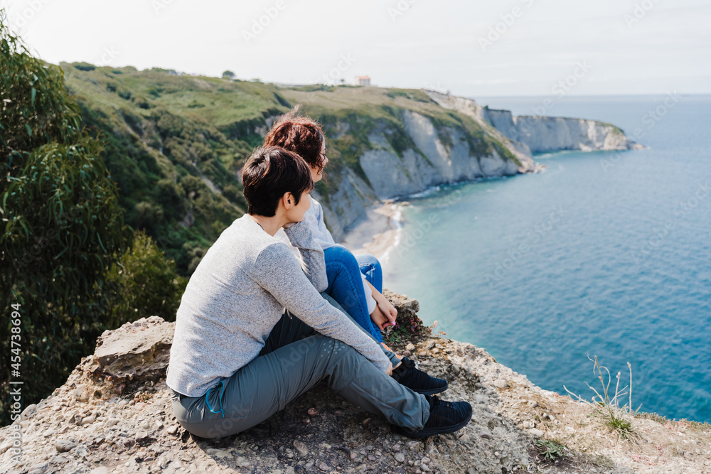 two women friends sitting and looking at beautiful sea landscape on top of the mountain. Friendship and nature concept