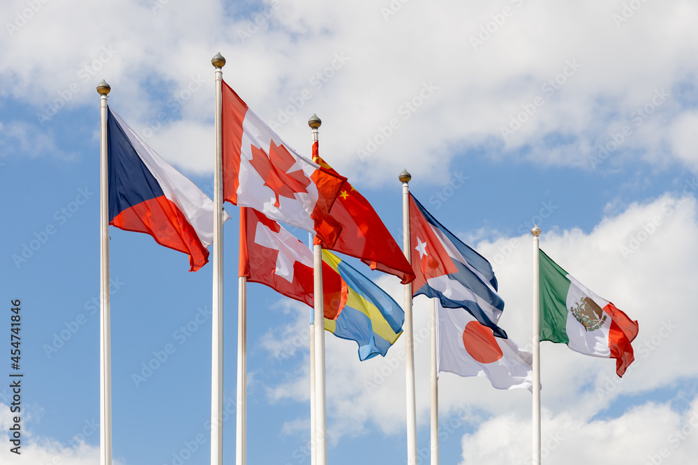 A few flags of various countries of the world flutter in the wind, against a cloudy sky. Flags of different states together - as a symbol of world cooperation. Various flags on flagpoles