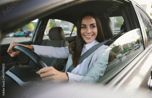 Beautiful happy successful businesswoman is driving a new modern car in good mood. Portrait cute female driver steering car with safety belt photo