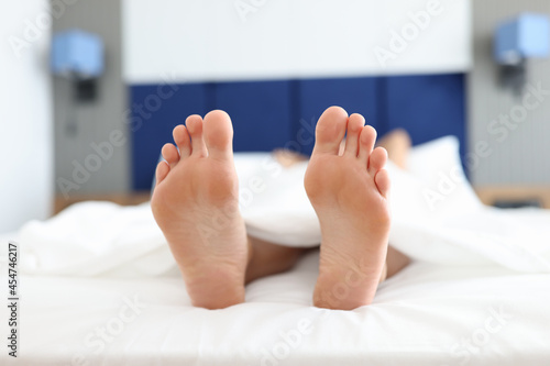 Female feet lying on white bed under covers closeup