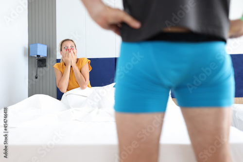 Canvas-taulu Surprised woman lying in bed and covering her mouth in front of man genitals