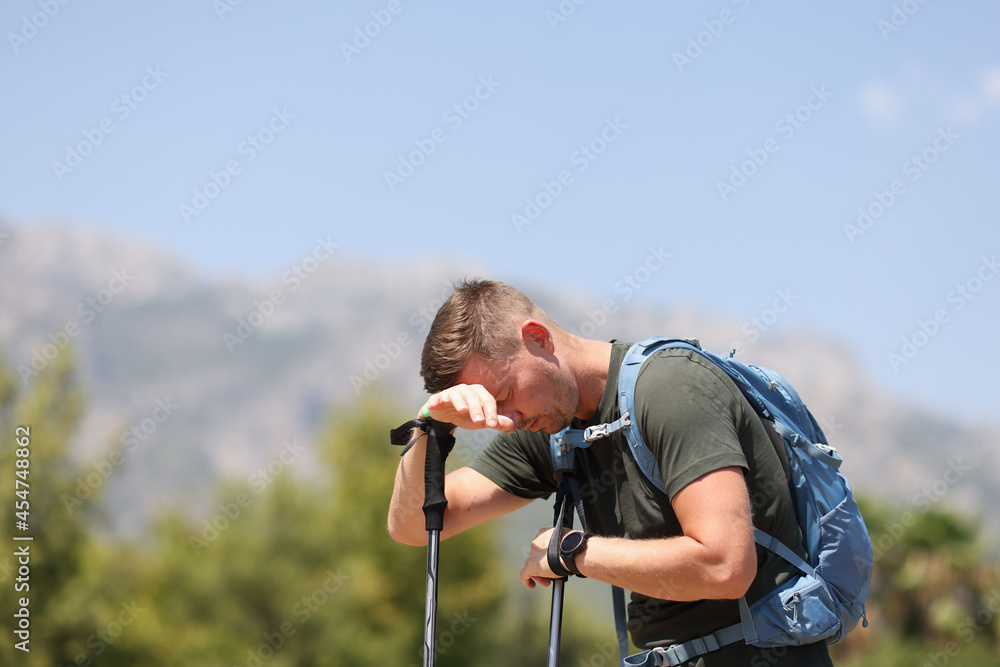 Tired man putting his head on walking sticks in mountains