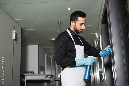bearded housekeeper in rubber gloves cleaning corridor in hotel